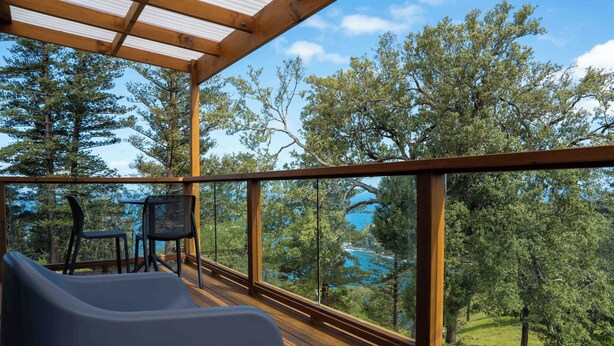 A wooden deck with a table and chairs, overlooking a scenic landscape with trees and a body of water.