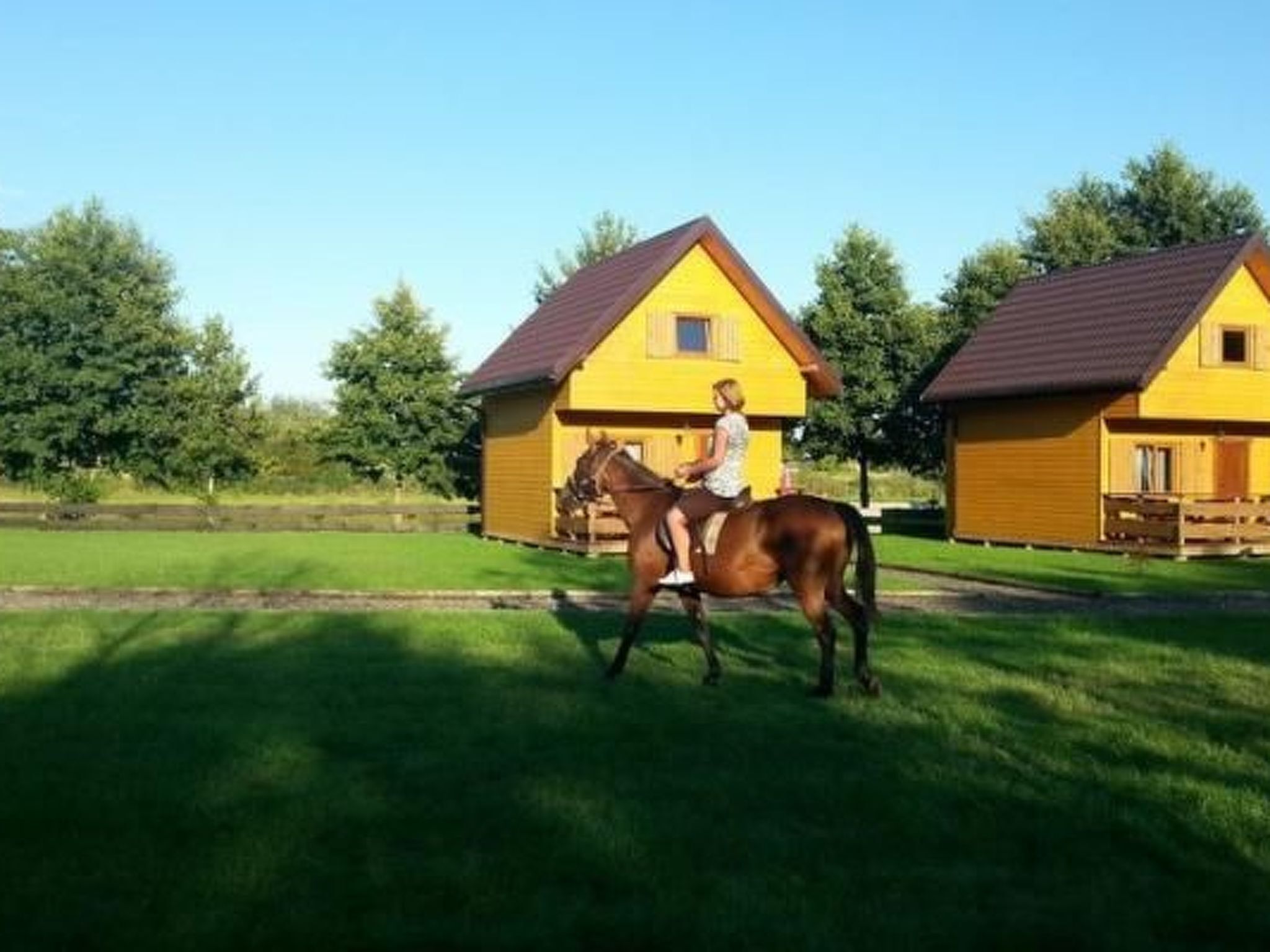 Eine Person reitet auf einem Pferd vor einem gelben Gebäude mit einem braunen Dach.