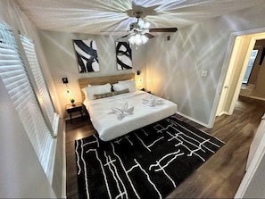 A bedroom with a bed, a ceiling fan, wall art, and a black and white rug.