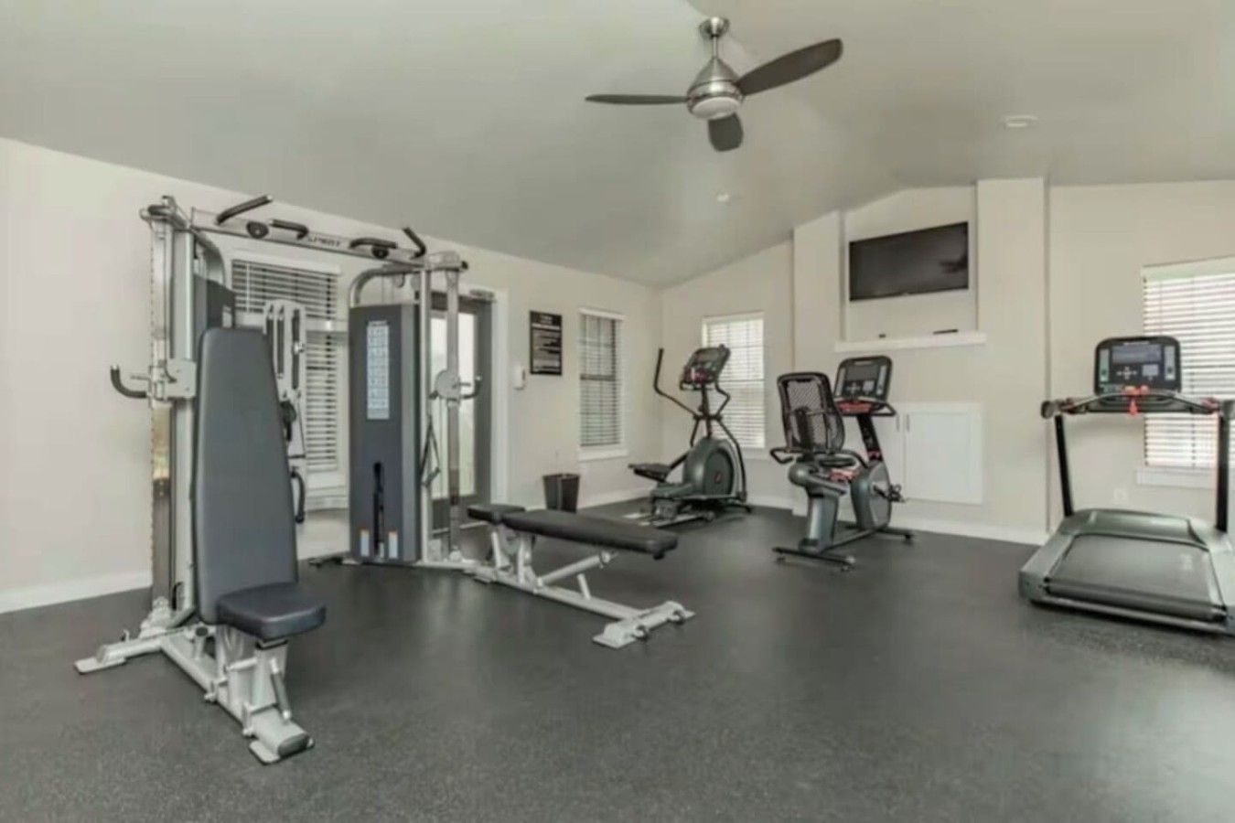 A gym with various exercise equipment including a bench press, elliptical machines, and a treadmill.