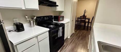 A compact kitchen with white cabinets, a black stove, a microwave, and a dining area with a table and chairs.
