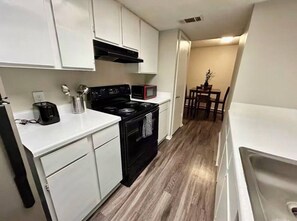 A compact kitchen with white cabinets, a black stove, a microwave, and a dining area with a table and chairs.