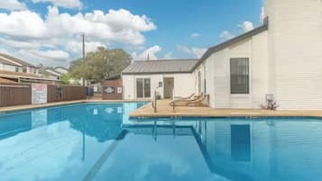 A swimming pool with lounge chairs, a small building with a door, and a fenced area with a sign.