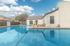 A swimming pool with lounge chairs, a small building with a door, and a fenced area with a sign.
