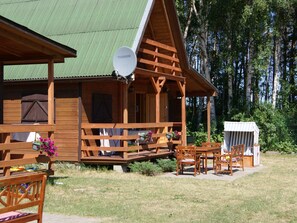 A wooden cabin with a green roof, a porch with wooden benches, and a small table with chairs. - Gemütliches Ferienhaus mit Garten und Terrasse by Interhome (Sarbinowo)