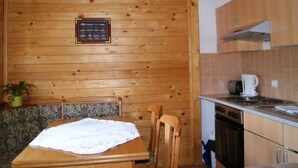 Un intérieur en bois comprenant une table à manger, des chaises, un luminaire fixé au mur, un coin cuisine avec une cuisinière et une plante en pot.