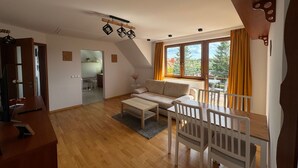 Un vaste espace de vie doté d’un plancher en bois, d’un canapé, d’une table à manger avec des chaises et d’une grande fenêtre agrémentée de rideaux.