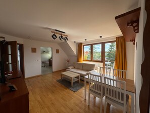 A spacious living area with a wooden floor, a sofa, a dining table with chairs, and a large window with curtains. - Wohnung mit Blick auf das Wasser by Interhome (Sarbinowo)