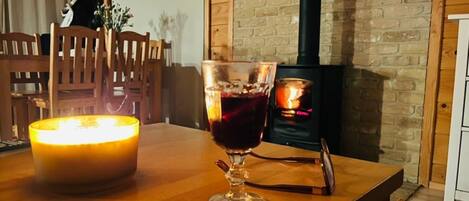 A cozy room with a wooden table, a lit candle, a glass of red wine, and a wood-burning stove.