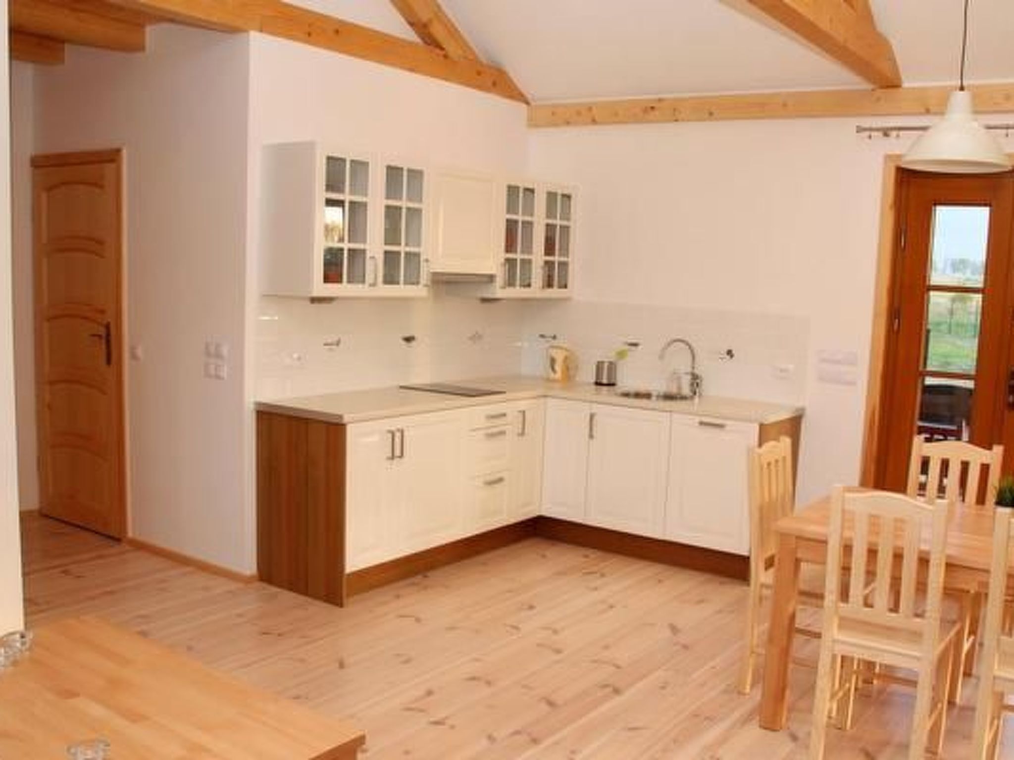 Une cuisine avec des meubles blancs, des poutres en bois et un coin repas comprenant une table et des chaises.