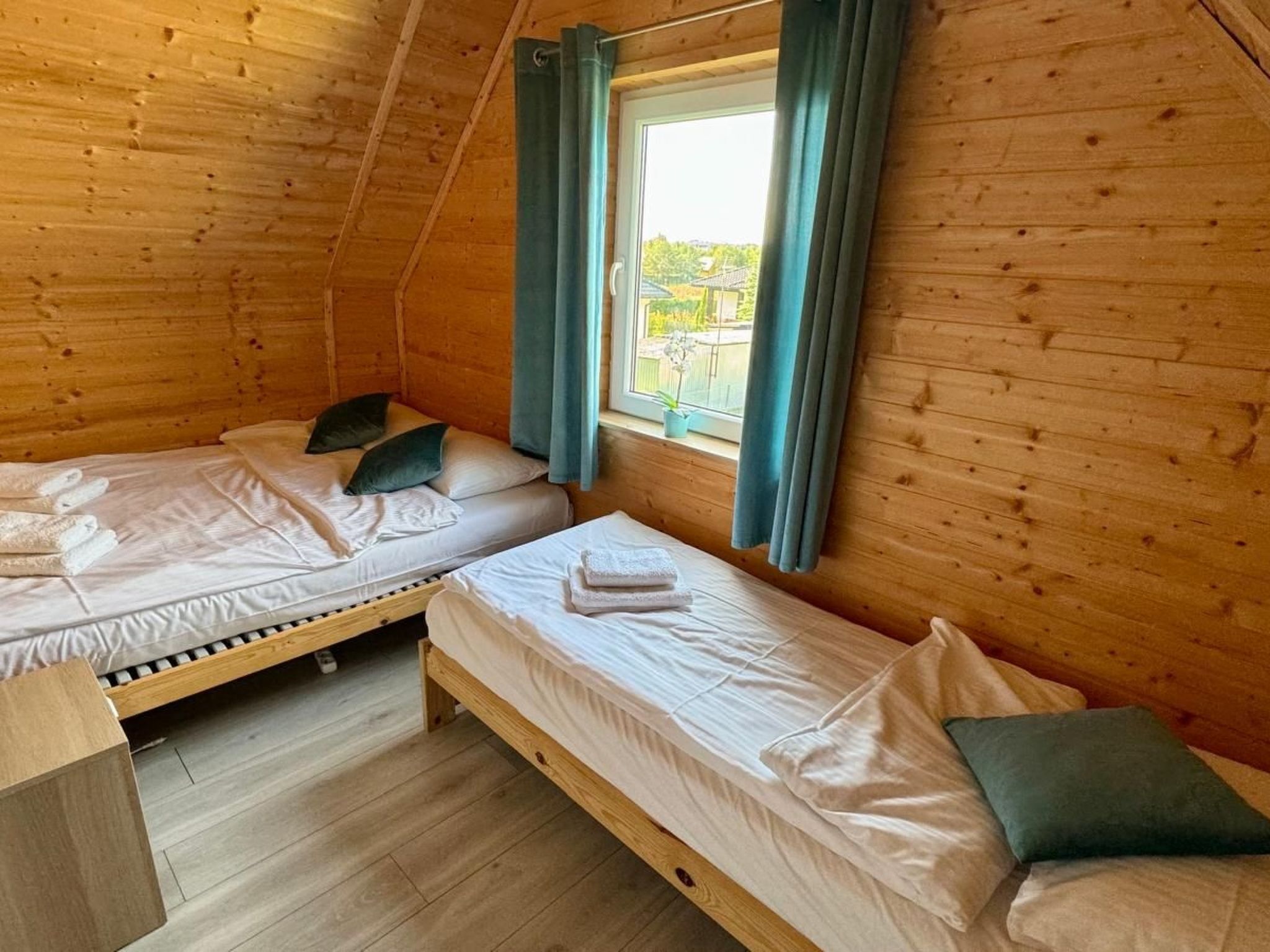 A cabin with two wooden bunk beds, a window with curtains, and a view of greenery outside.
