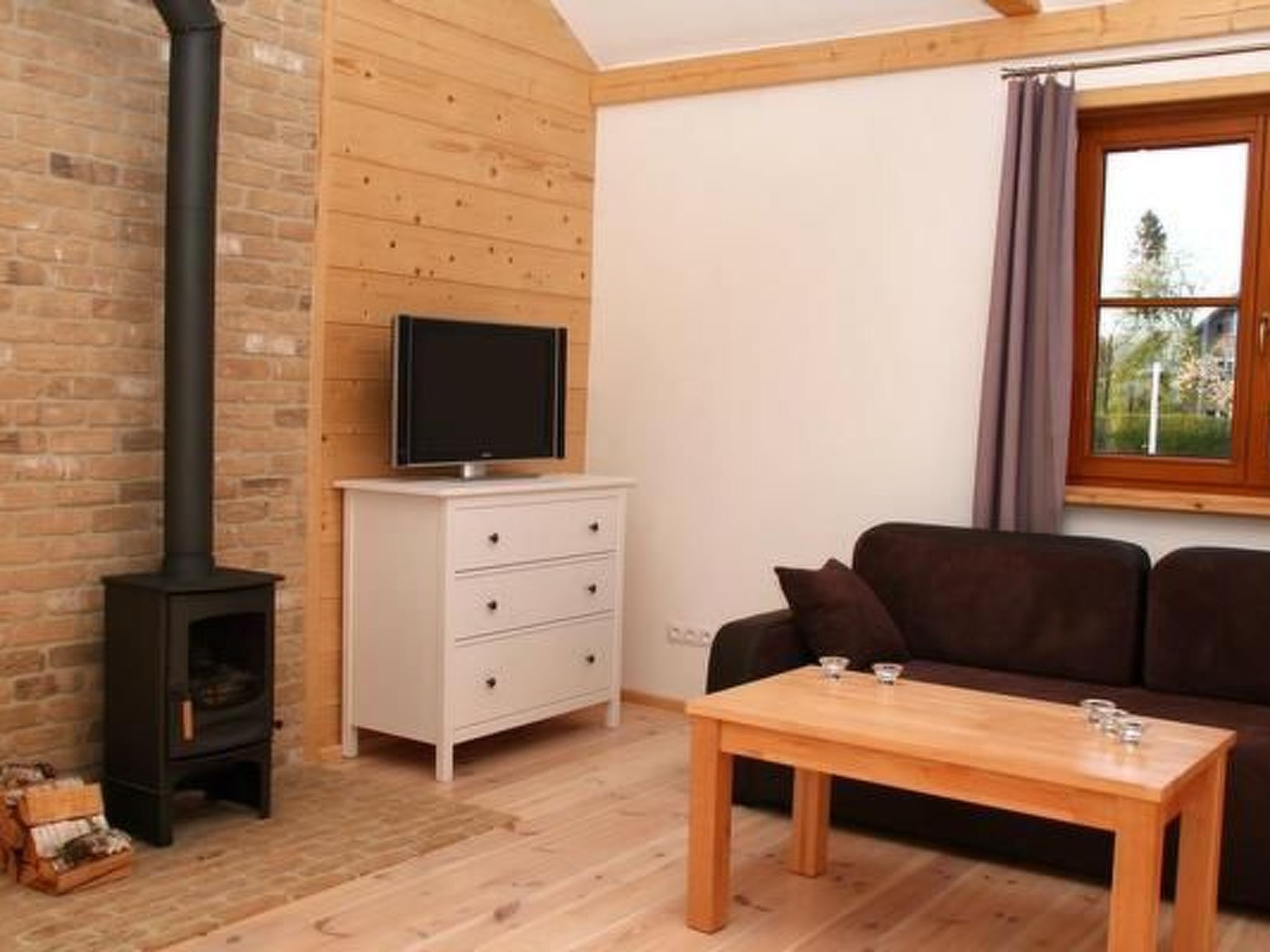 Ein gemütliches Wohnzimmer mit Kamin, einer weißen Kommode, einem braunen Sofa und einem Holztisch.