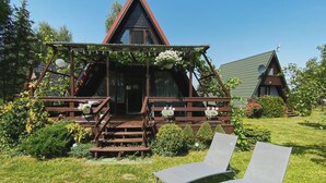 A wooden cabin with a triangular roof, a porch with steps, and two lounge chairs in the foreground.
