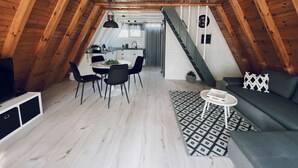 A cozy attic bedroom with a wooden ceiling, a dining area with a table and chairs, a sofa, and a patterned rug.