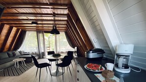 A cozy loft-style room with a dining area, a sofa, and a kitchen counter with a coffee maker and watermelon slices.