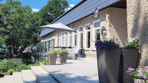 A building with a stone facade, large windows, and a covered outdoor seating area with umbrellas. - Beach Club-Häuser direkt am Strand by Interhome (Dziwnówek)
