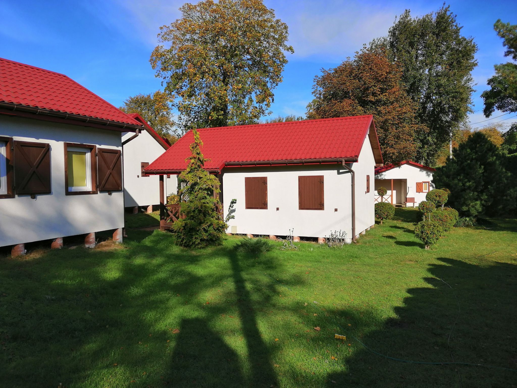 Une rangée de petites maisons blanches aux toits rouges, entourées d’herbe verte et d’arbres.