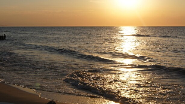 A beach scene with the sun setting over the ocean, waves gently lapping at the shore.