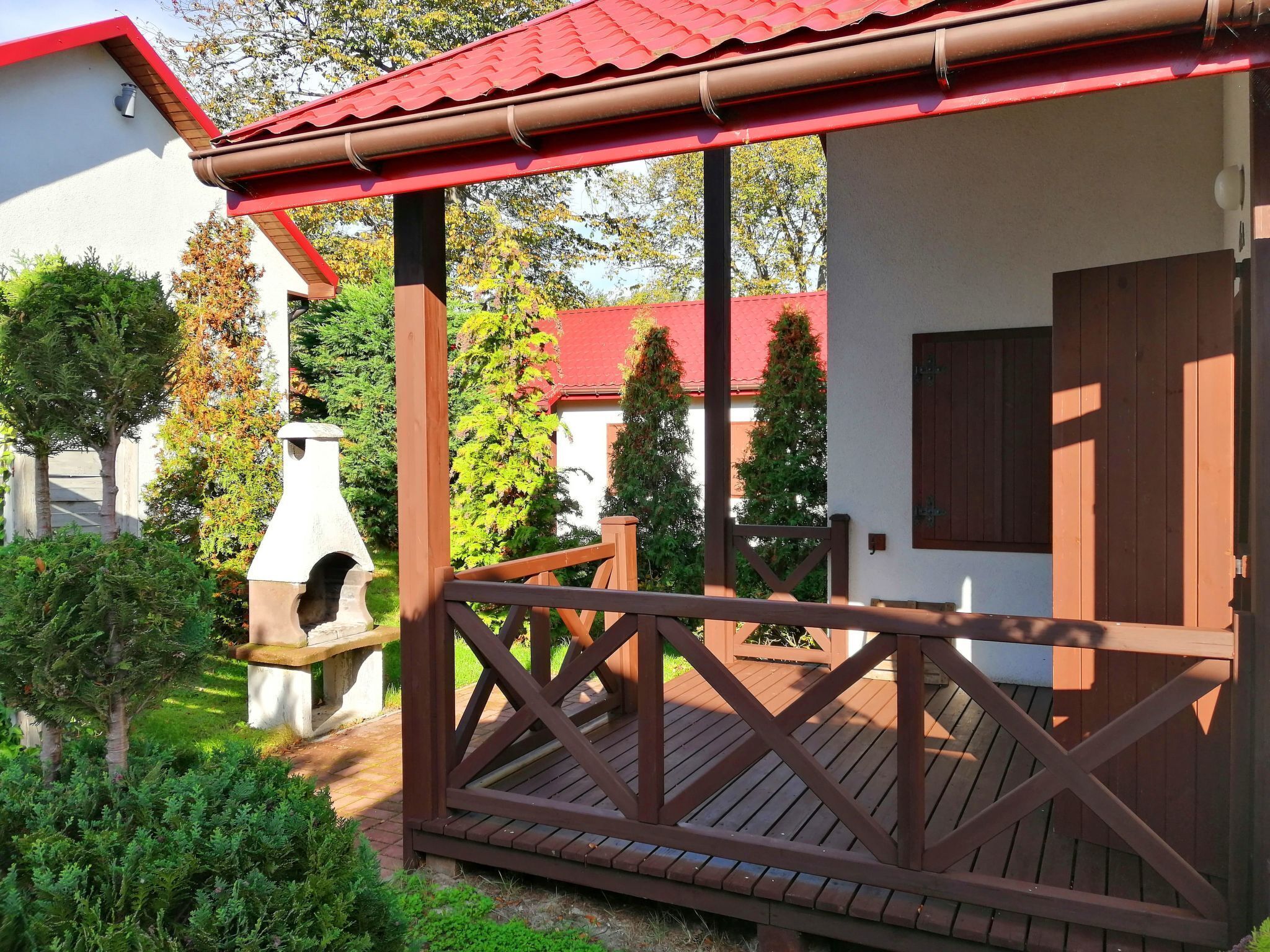 Eine Holzterrasse mit rotem Dach, einer Steinsitzbank und einer Holztür.