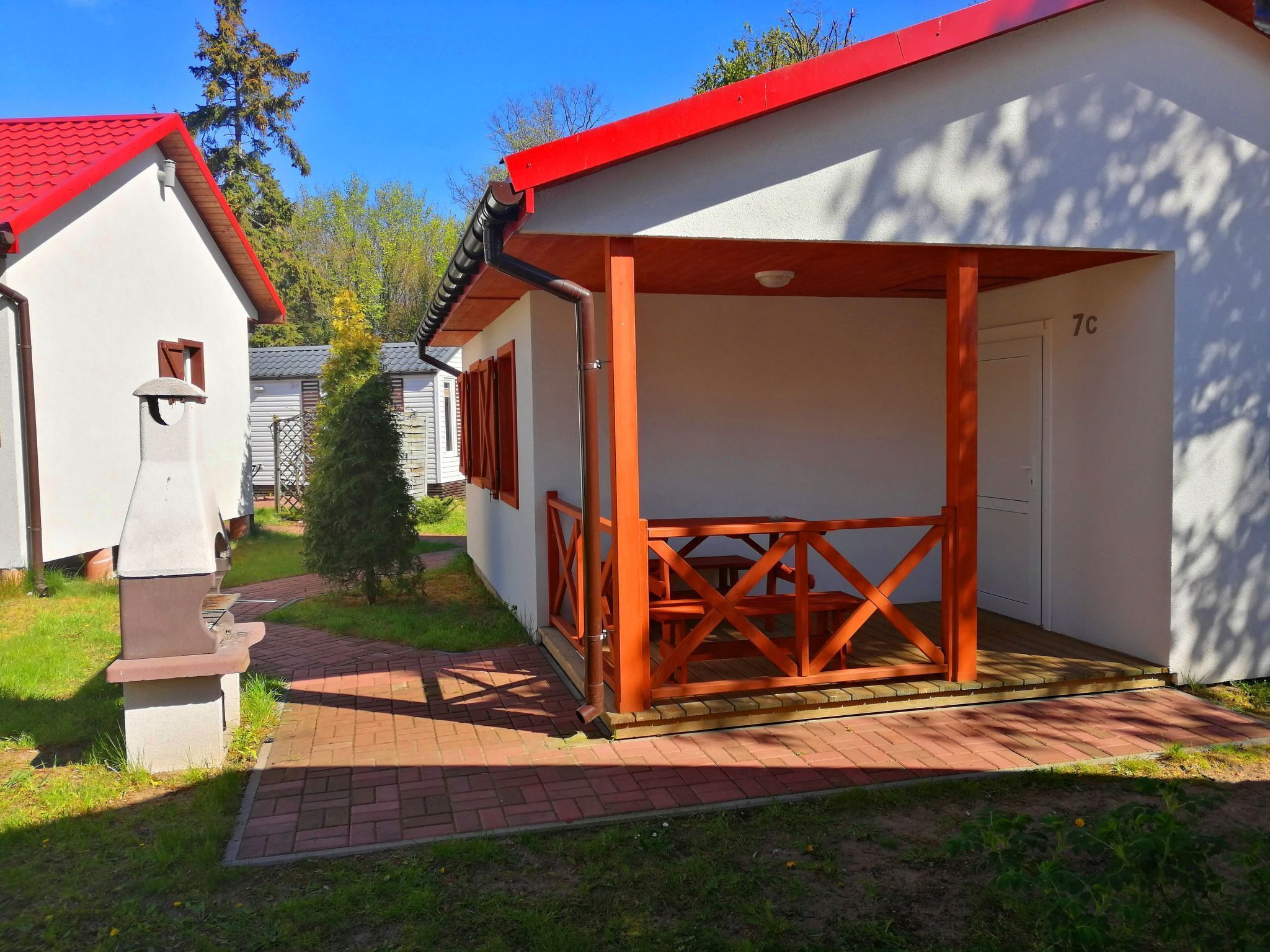 A small, single-story building with a red roof and white walls, featuring a covered outdoor seating area with a wooden table and chairs.