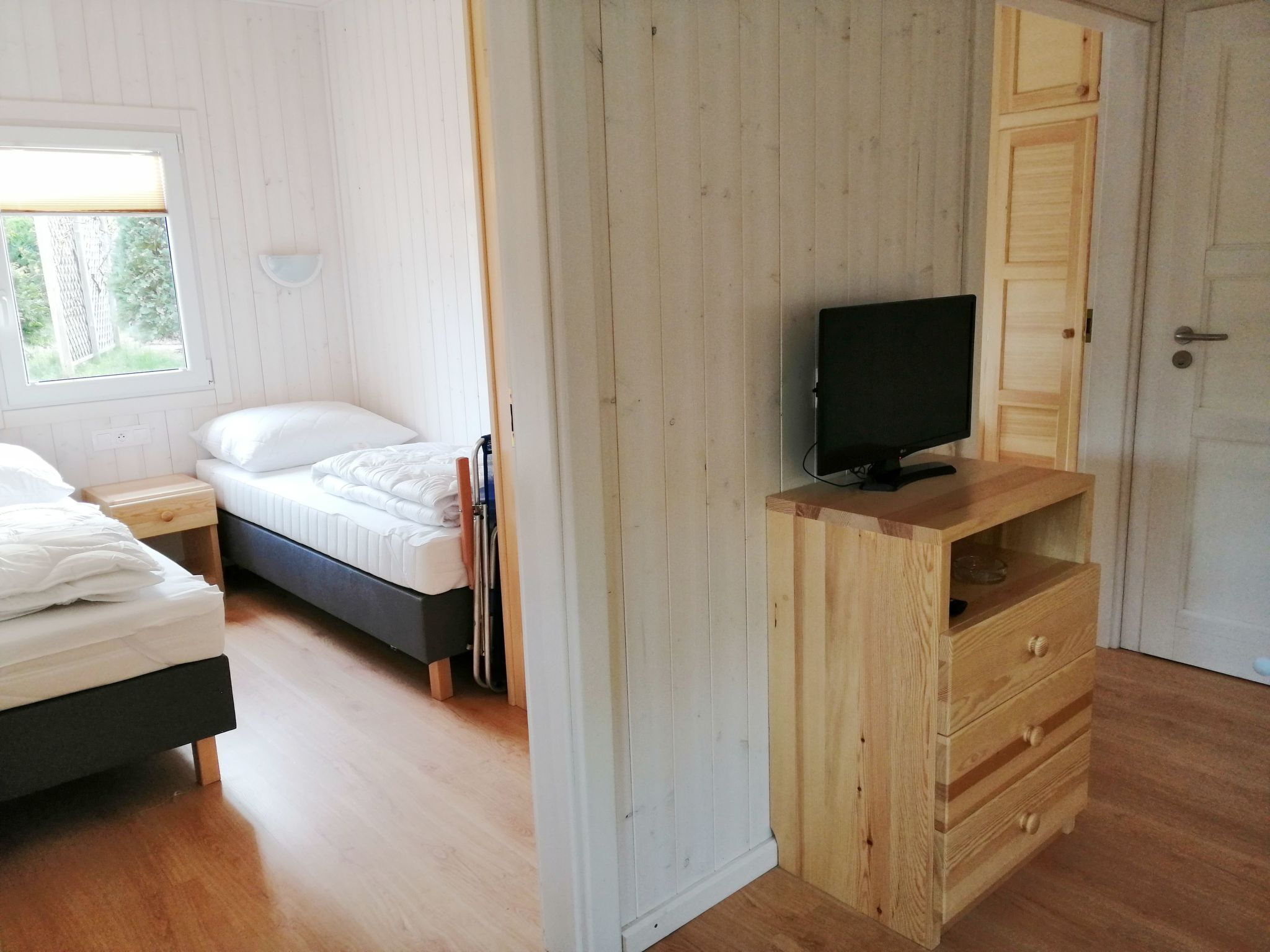 A bedroom with a bed, bedside tables, a television on a wooden stand, and a door.