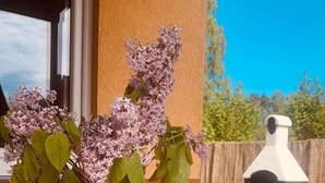 Ett utomhusbord med en bok, ett glas iste, ett glas iskallt kaffe och en vas med syrenblommor.