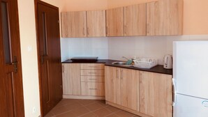 A compact kitchen with wooden cabinets, a black countertop, a sink, a kettle, and a white refrigerator. - Ferienanlage Belona/A1 by Interhome (Niechorze)