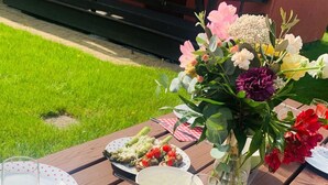 A picnic setup with plates of sausages and a bowl of soup, a vase of flowers, and glasses of white wine on a wooden table. - Appartements mit einem Wohn-,Ess- und Schlafraum und kleinem Balkon für vier Pe by Interhome (Niechorze)