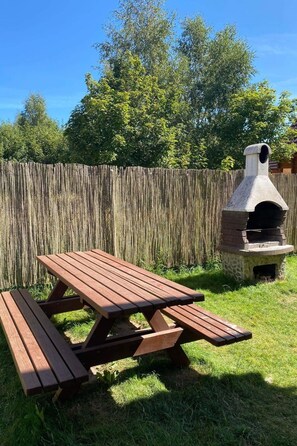 A picnic table and a stone-built outdoor oven in a grassy backyard with a wooden fence in the background. - Appartement mit einem Wohn-,Ess- und Schlafraum und kleiner Terrasse für vier P by Interhome (Niechorze)