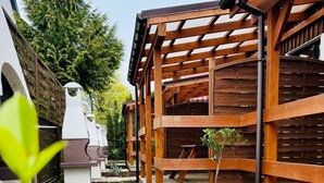 A wooden pergola structure with a stone base, surrounded by a gravel pathway and small plants. - Bootshaus mit Schwimmbad by Interhome (Rewal)