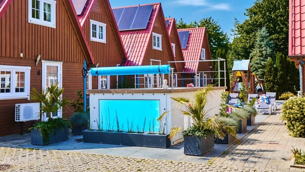 A row of red-roofed wooden houses with solar panels, a blue awning, and potted plants. - Bootshaus mit Schwimmbad by Interhome (Rewal)