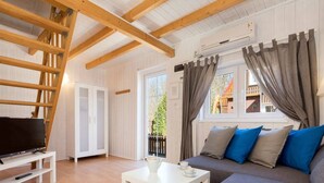 A cozy living room with a TV on a white stand, a white coffee table, a grey sofa with blue cushions, and a wooden ladder against the wall. - Bootshaus mit beheiztem Pool by Interhome (Rewal)