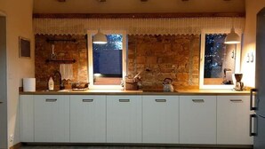Una cucina con parete in pietra, una finestra con tende di pizzo e un bollitore sul piano di lavoro.
