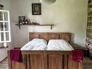 Una cama de madera con cabecera, un estante encima y una ventana a la izquierda.