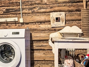 A rustic cabin interior with a washing machine, a small table with a decorative item, and a wall adorned with a patterned border.