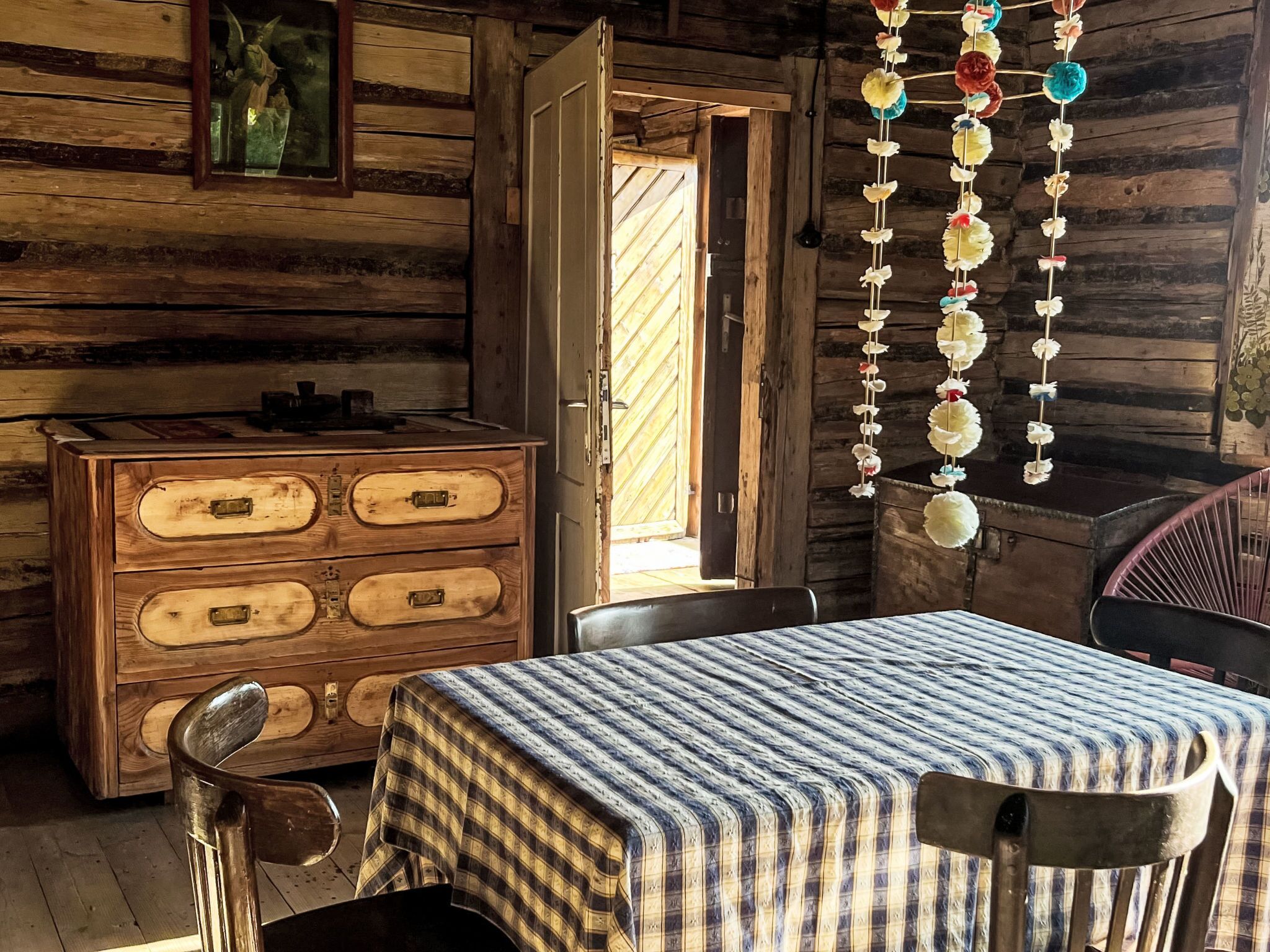 A rustic wooden cabin interior with a wooden dresser, a table with a checkered tablecloth, and a hanging decoration.