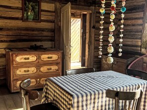 A rustic wooden cabin interior with a wooden dresser, a table with a checkered tablecloth, and a hanging decoration.
