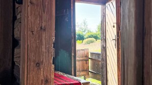 A rustic wooden room with a bed and a view of a wooden fence and greenery outside.