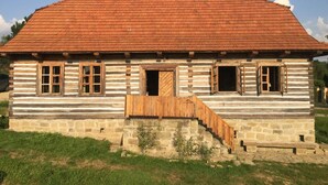 A log cabin with a wooden staircase leading to the entrance, a red-tiled roof, and a stone foundation.