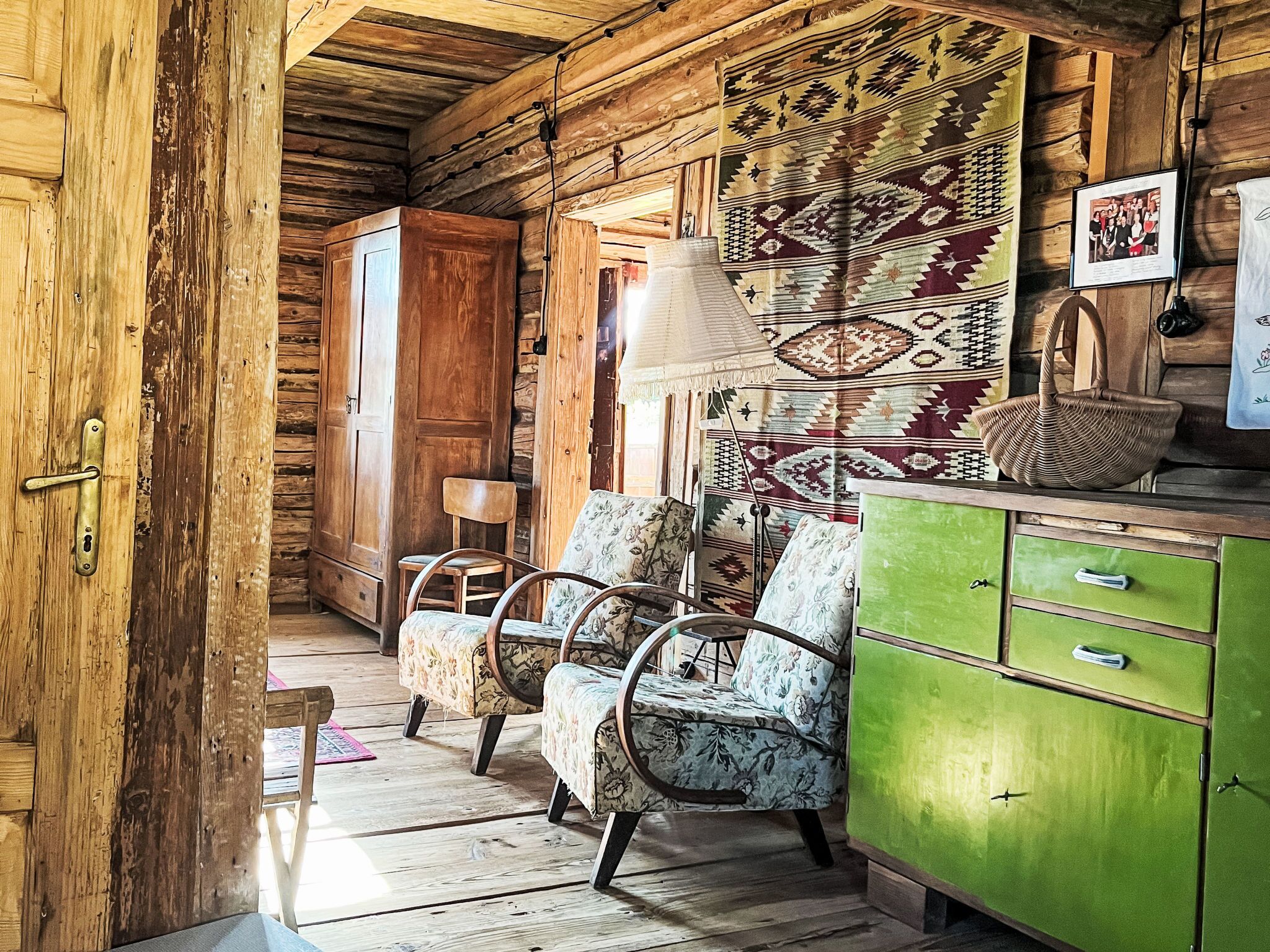 A rustic interior with wooden walls, a green cabinet, floral-patterned chairs, and a woven rug.