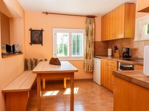 A compact kitchen with wooden cabinets, a dining table, and a window with curtains. - in der Nähe von Thermalbad by Interhome (Mala Nedelja)