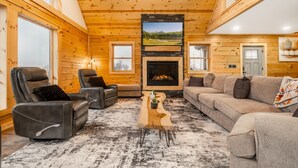 A log cabin interior with a fireplace, leather recliners, a sofa, and a wooden coffee table. - Brand New Luxury 7 BR Cabin w Hot Tub, Game Room (McHenry)