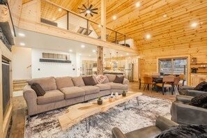 Un amplio salón con un gran sofá modular, una mesa de centro de madera y un techo alto con vigas de madera a la vista.