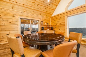 Interior de madeira com mesa redonda e cadeiras, uma janela e vista para o exterior.