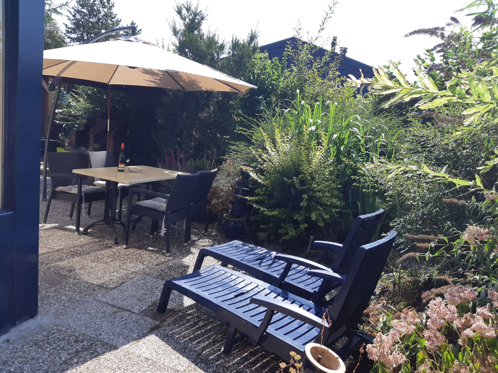 Een terras buiten met een tafel en stoelen, omringd door groen en een pergola met een zonnedak.