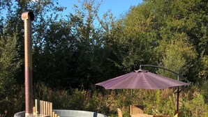 Ein Whirlpool mit Holzfassade, umgeben von einer Holzterrasse, einem violetten Sonnenschirm und Holzstühlen.