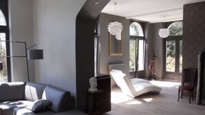Ein modernes Wohnzimmer mit einer Ledersofa, einem weißen Sessel, einer Stehlampe und einem großen Fenster mit Blick auf Grünflächen.