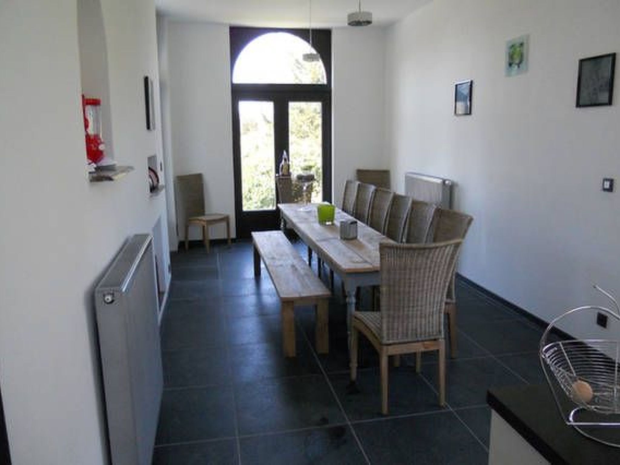 A dining area with a wooden table and chairs, a bench, a radiator, and a window with a view.
