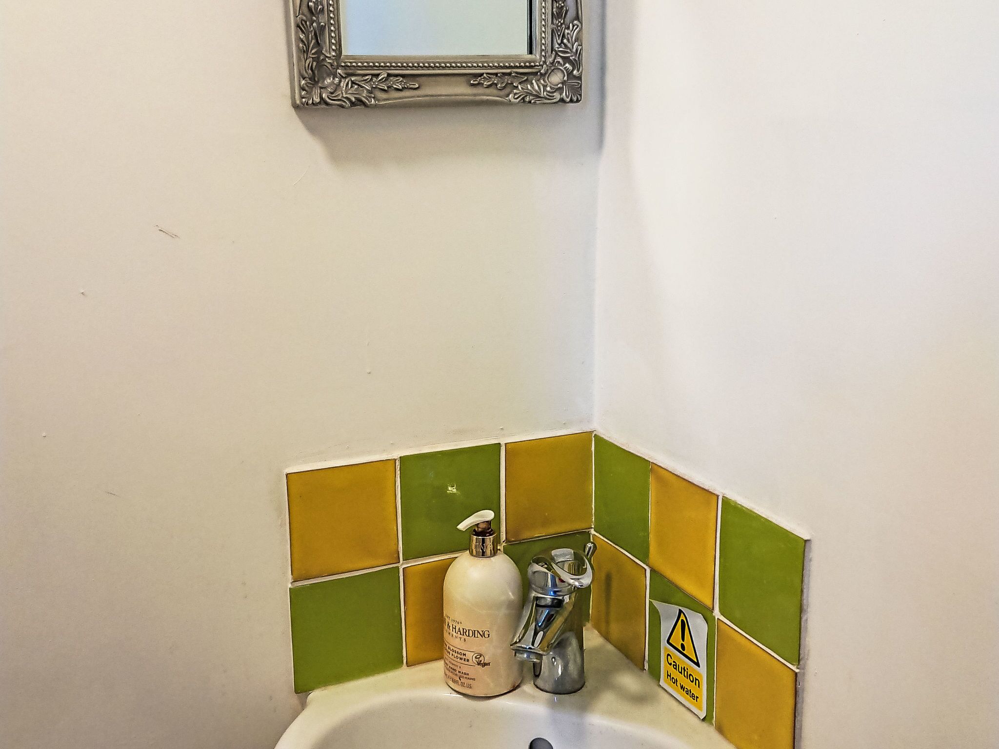 Rincón de baño con un lavamanos, dispensador de jabón y un letrero de precaución.