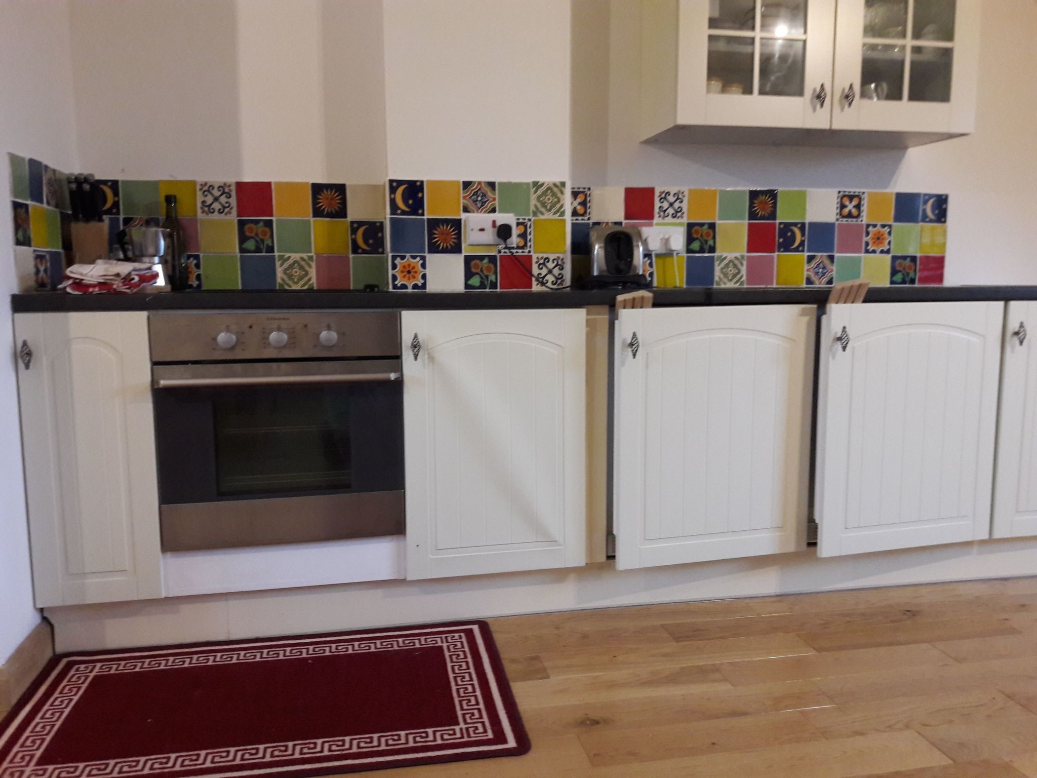 A kitchen with white cabinets, a stainless steel oven, and colorful tiles on the backsplash.
